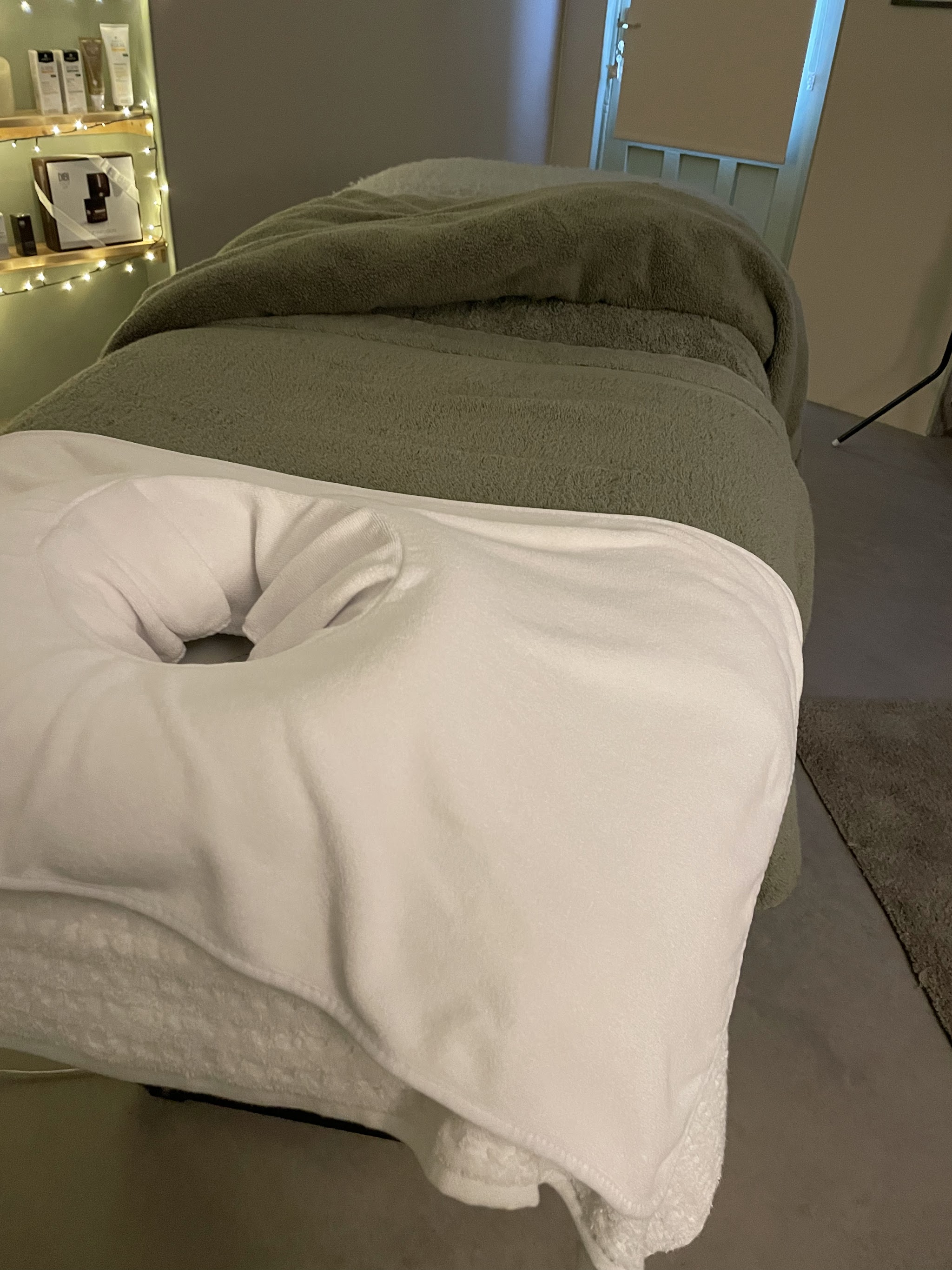 The treatment couch made up with a sage blanket, with fairy-lit shelves behind
