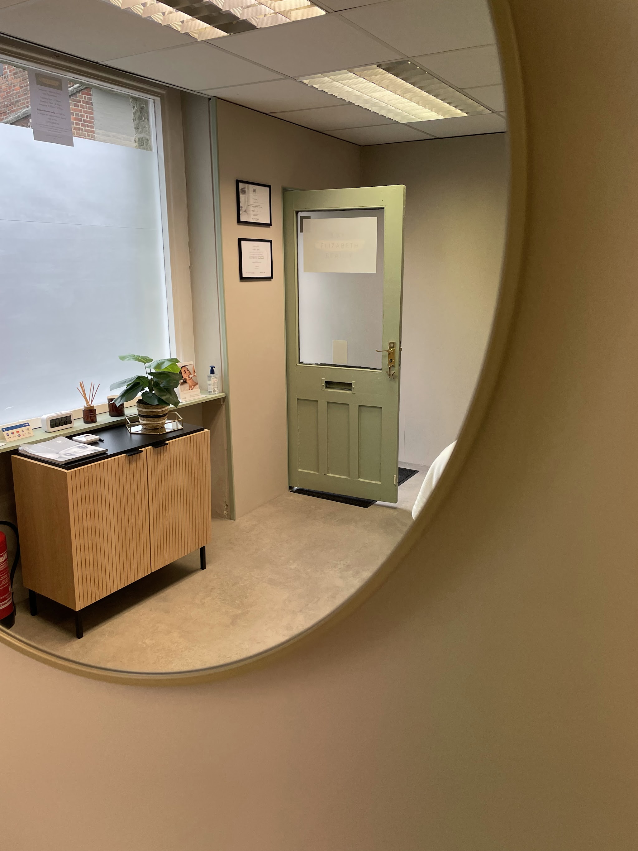 The treatment room reflected in the round mirror, with the sage door and a plant