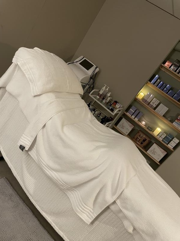 The couch made up with white towels beside shelves of skincare